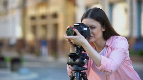 Улыбающаяся женщина-фотограф фокусирует объектив камеры на улице, фотосессии — стоковое видео