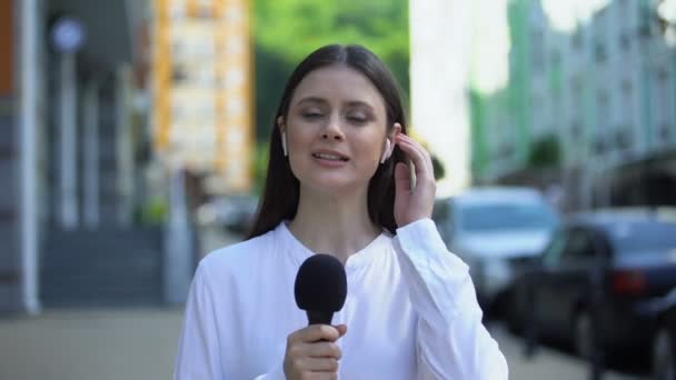 Жінка-репортер з мікрофоном у навушниках, що розмовляють на камеру, щоденні новини — стокове відео