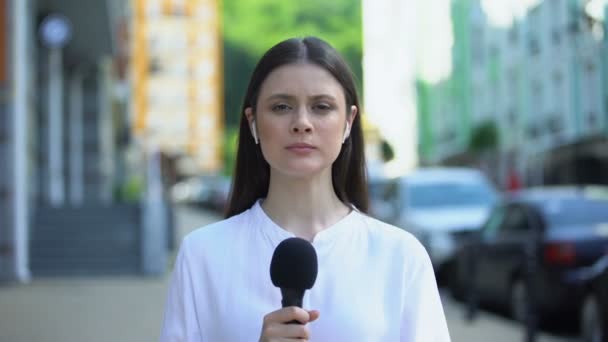 Серьезная женщина-репортер с микрофоном перед камерой, срочные новости — стоковое видео