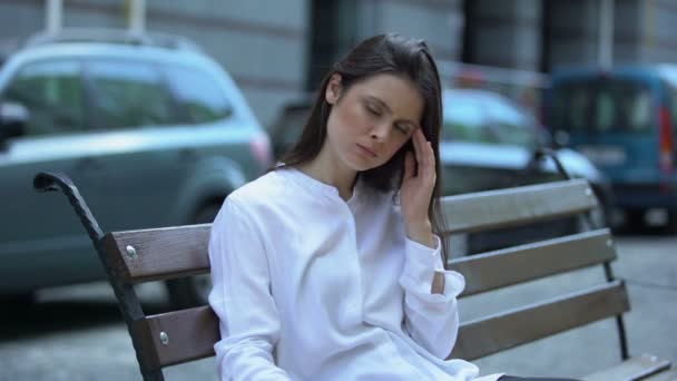 Mujer agotada sentada en el banco, sufriendo de dolor de migraña, problemas de salud — Vídeos de Stock