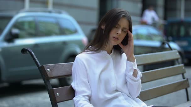 Tired lady sitting on bench, suffering from head ache, meteorological dependence — Stock Video