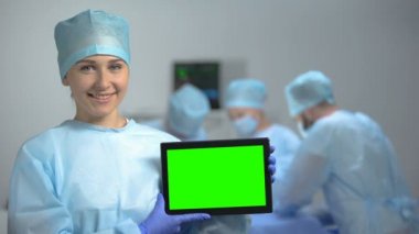Ameliyat sırasında yeşil ekranlı tablet Pc tutan gülümseyen hemşire, hastane reklamı