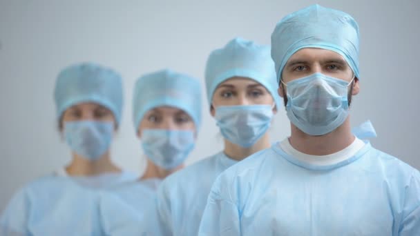 Профессиональная команда хирургов в маске и униформе смотрит на камеру, работу в больнице — стоковое видео
