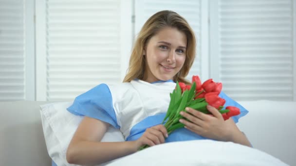 Mujer sonriente sosteniendo racimo de tulipanes en el hospital, presente después del parto — Vídeos de Stock