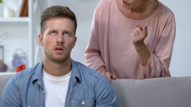 Zralá matka hlodá v podrážděném dospělém synovi, který sedí na pohovce, rodinné konflikty — Stock video