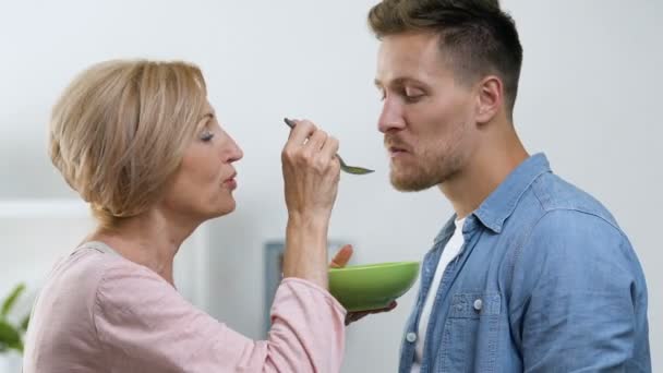 Overprotective mother feeding her adult son with spoon, relations in family — Stock Video