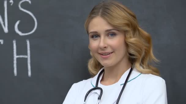 Atrakcyjny żeński lekarz stojący i uśmiechnięty do krzywka, womans ochrona zdrowia — Wideo stockowe