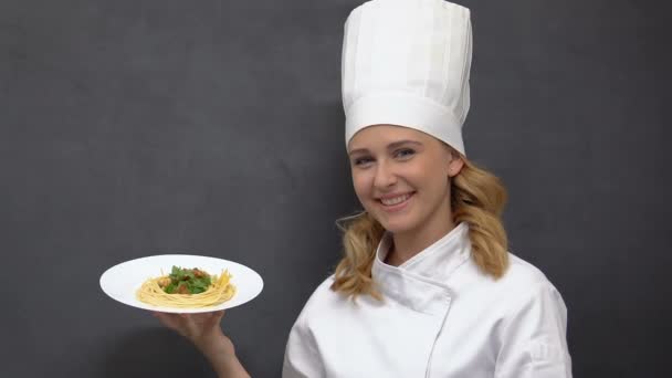 Cocinera feliz sosteniendo plato con pasta y sonriendo, invitando al restaurante — Vídeos de Stock