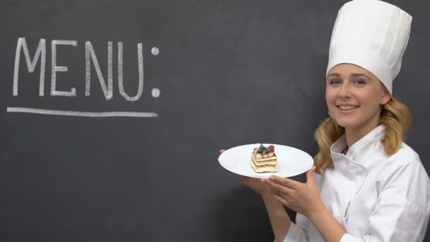 Дружелюбная женщина-повар держит торт на тарелке, меню написано на доске, horeca — стоковое видео
