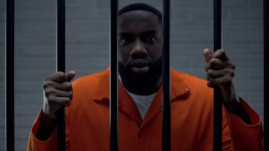 Korkmuş afro-amerikan mahkum parmaklıklar tutan, korku ile kameraya bakıyor