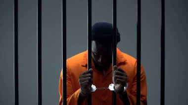 Hapishane parmaklıkları tutan kelepçeli afro-Amerikan suçlusinirlendi, geçmişten pişman