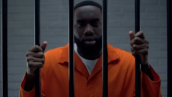 Prisionero negro sosteniendo barras y mirando a la cámara, castigo traficante de drogas — Foto de Stock