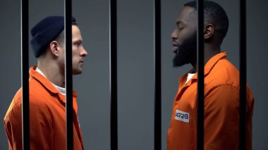 Afro-american and caucasian inmates looking at each other in cell, conflict clipart