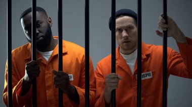 Afro-Amerikan ve kafkas suçlular hapishane parmaklıkları tutan ve kamera bakarak
