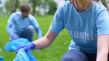 Genç kadın gönüllü parkta çöp toplama, kamera da gülümseyerek, doğayı kurtarmak