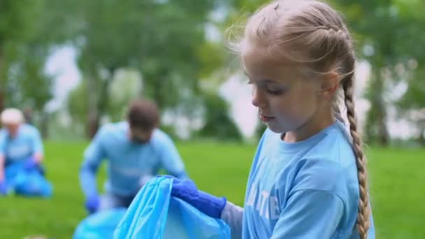 公園でゴミを集める小さなボランティアの女の子、カメラに微笑む、自然ケア — ストック動画