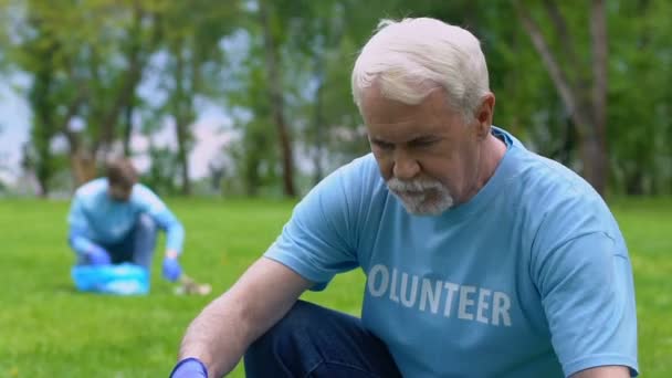 Ältere männliche Freiwillige sammeln Müll im Park, lächeln in die Kamera, Altruismus — Stockvideo