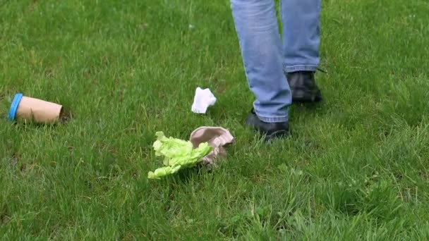 Чоловік-доброволець збирає сміття після того, як безвідповідальний чоловік кидає паперову чашку на газон — стокове відео
