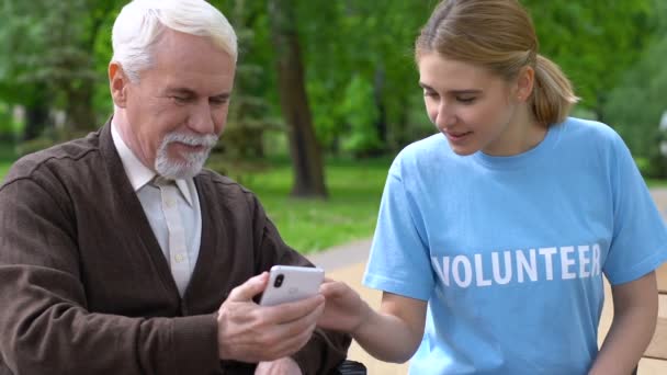 Amable voluntaria ayudando a pensionista en silla de ruedas uso de teléfono inteligente aplicación de caridad — Vídeo de stock