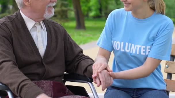 Sonriente joven voluntario que apoya al anciano discapacitado en el parque, ayudando a jubilado — Vídeo de stock