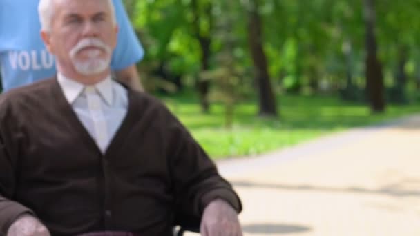 Женщина-волонтер гуляет с одиноким инвалидом-колясочником в парке, поддерживает — стоковое видео