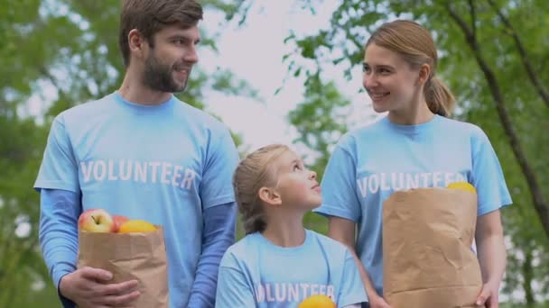 Joyeux bénévoles famille avec des pommes sacs en papier souriant à la caméra, charité — Video