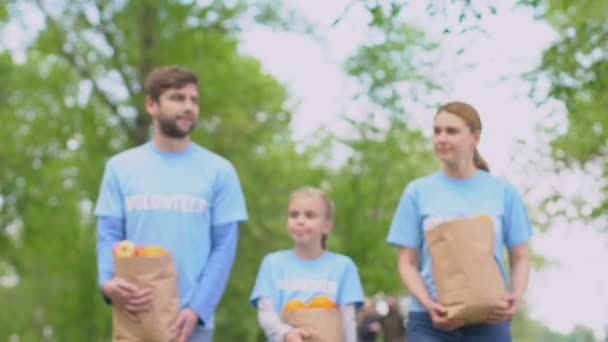 Lachende vrijwilligers familie met vruchten papieren tassen wandelen in Park liefdadigheid project — Stockvideo