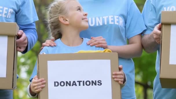 Команда дорослих добровольців з дитиною тримає подарункові коробки і посміхається, благодійність — стокове відео
