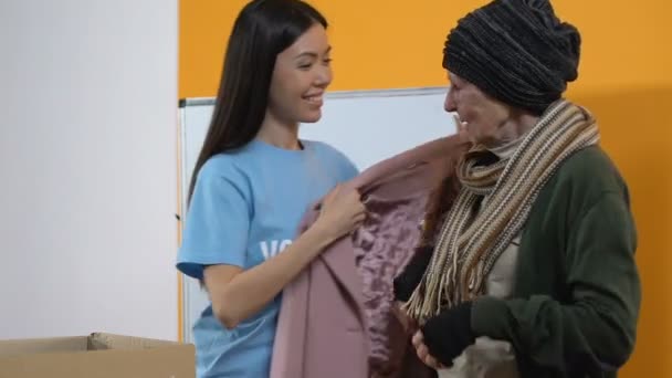 Jonge vrouwelijke vrijwilliger geven winterjas voor arme dakloze lachende vrouw, hulp — Stockvideo