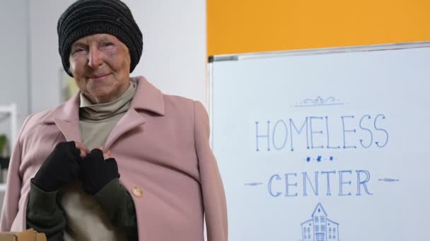 Poor homeless woman in donated warm clothing looking to camera in support center — Stock Video