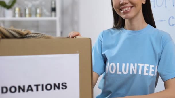 Smiling volunteer standing near boxes with donated clothing, homeless assistance — Stock Video