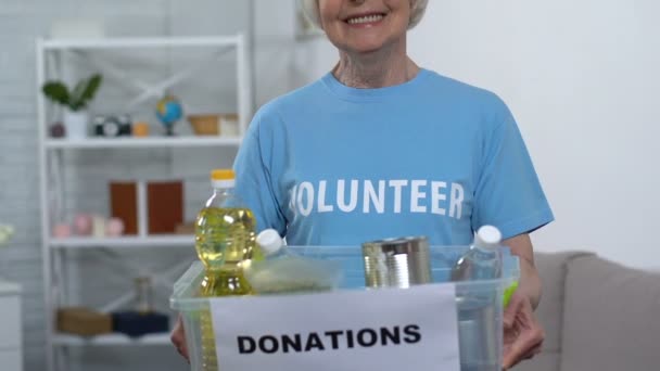 Idosos senhora voluntária segurando caixa com comida, olhando para câmera e sorrindo, ajuda — Vídeo de Stock