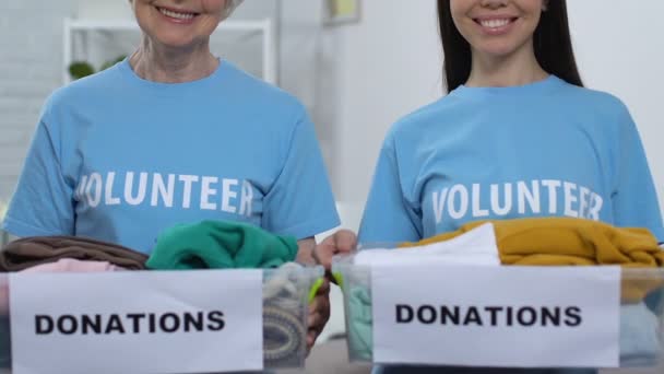 Amables damas voluntarias mostrando cajas con ropa a donaciones de cámaras para pobres — Vídeo de stock