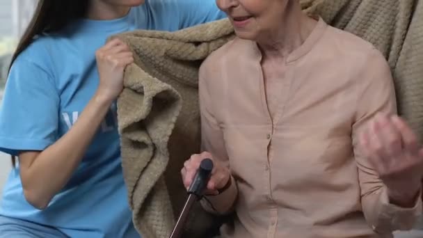 Уважний молодий волонтер, який охоплює старшу жінку з пледом, допомогою і турботою — стокове відео