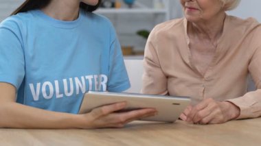 Genç gönüllü ve emekli bayan tablet kaydırma ve kamera, bankacılık gülümseyerek