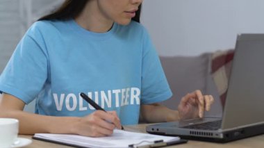 Gülümseyen gönüllü dizüstü bilgisayar ve yazılı listede kamera bakarak veri karşılaştırarak