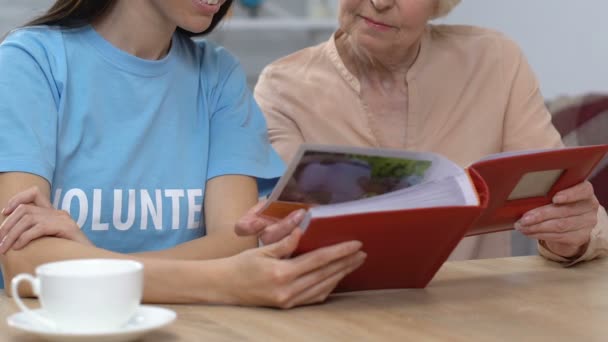 Vieja mostrando fotos familiares a jóvenes voluntarios pasando tiempo libre juntos — Vídeos de Stock