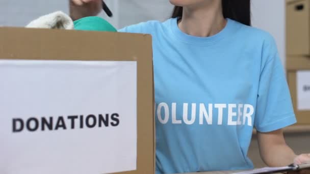 Mujer voluntaria haciendo lista de ropa donada y sonriente, donaciones de caridad — Vídeos de Stock