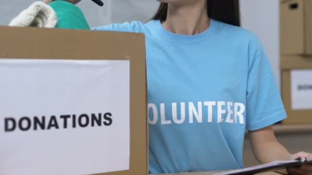 Jeune femme bénévole regardant à travers les vêtements donnés dans la boîte et souriant charité — Video