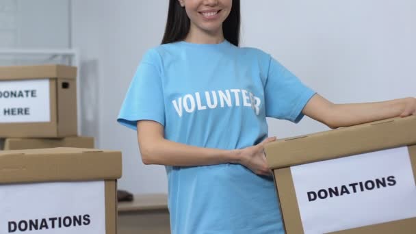 Mujer de corazón abierto voluntario sosteniendo caja de donación y sonriendo a la cámara, cuidado — Vídeo de stock