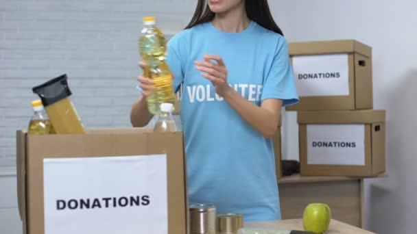 Lady volunteer packing food in cardboard boxes donations for low-budget families — Stock Video