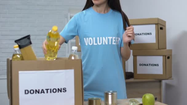 Добрий доброволець упаковує продовольчі товари в коробки і посміхається камері, пожертвування — стокове відео