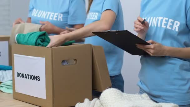 Voluntarios empacando ropa donada en cajas, supervisor sosteniendo lista de verificación, cuidado — Vídeo de stock