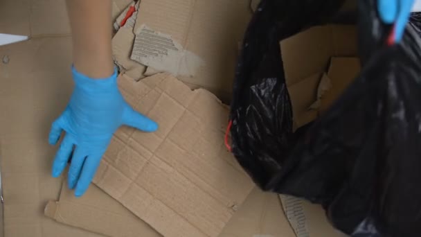 Человек в защитных перчатках собирает рванный картон в пластиковый пакет, перерабатывает — стоковое видео