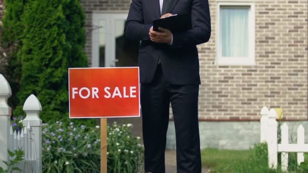 Sorridente vestito broker maschile in piedi vicino per la vendita segno fuori casa, occupazione — Video Stock