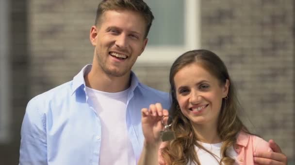 Heureux mari et femme montrant la caméra souriante clé à l'extérieur de la maison, déménagement — Video