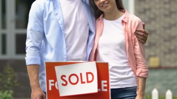 Jeune mari et femme près vendu signe extérieur maison sourire caméra, déménagement — Video