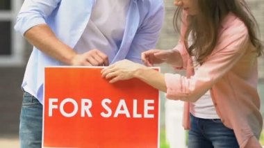 Genç adam ve kadın ev bahçesinde satılık işareti ayarı, genç aile tehcir