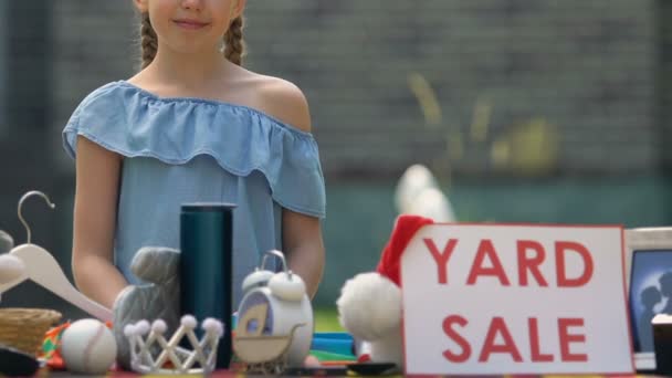 Signe souriant de vente de cour de fille sur la table, enfant vendant des choses inutilisées, quartier — Video