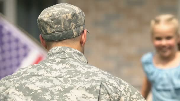 Счастливая дочь с американским флагом обнимает отца в военной форме, возвращение домой — стоковое видео